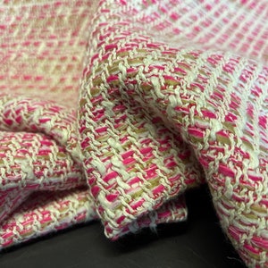 May include: Close-up of a pink, white and beige tweed fabric with a woven texture.