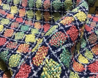 May include: Close-up of a blue fabric with a woven pattern of colorful squares. The squares are made of pink, yellow, and green threads.