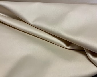 May include: A close-up of a smooth, ivory-colored fabric with a subtle sheen. The fabric is folded in a way that shows its drape and texture.
