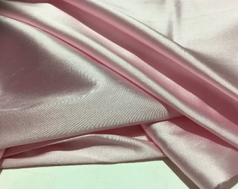 May include: A smooth, silky fabric in a pale pink color. The fabric is folded and draped, showcasing its luxurious texture.