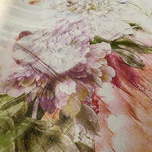 Puede incluir: Una tela blanca con un estampado floral que presenta flores rosas y moradas con hojas verdes. El fondo es beige claro con una textura sutil de veta de madera.