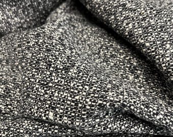 May include: Close-up of a textured fabric with a woven pattern. The fabric is primarily black and white, with a speckled appearance. The material is folded, showing depth and dimension. The overall texture appears soft and possibly suitable for clothing or upholstery.