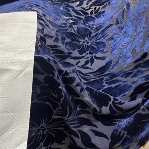May include: A close-up of a navy blue sheer fabric with a floral pattern. The fabric is soft and has a velvety texture.