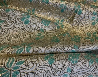 May include: Close-up of a white fabric with a silver and teal floral pattern. The fabric has a subtle shimmer and a textured surface.