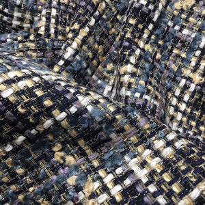 Puede incluir: Primer plano de una tela texturizada con un patrón tejido en tonos azules, blancos, dorados y morados.