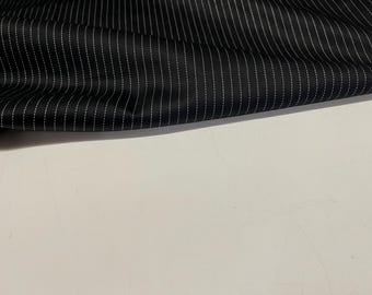May include: Black fabric with vertical white pinstripes. The fabric is slightly rippled, creating soft shadows. The pinstripes are evenly spaced and appear to be stitched. The background is a plain white surface.