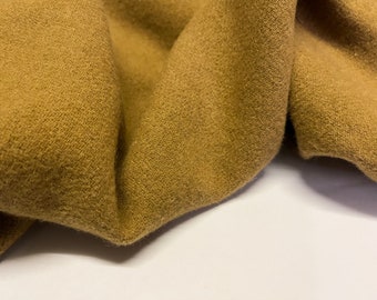 May include: Close-up of a soft, brown fabric with a textured surface. The fabric is folded and draped, showing its texture and drape.