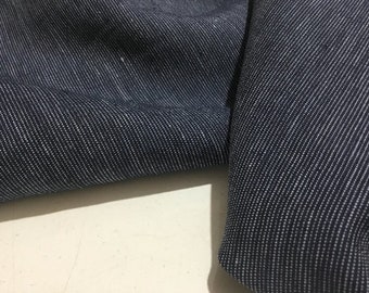 Op de afbeelding: Close-up van een donkerblauwe denim stof met een subtiel wit streepjespatroon. De stof is dubbelgevouwen, waardoor de textuur en de weving zichtbaar zijn.