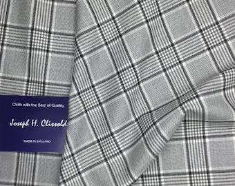 May include: Close-up of a gray and white plaid fabric with black accent lines. The fabric is folded, showing the texture and pattern. A blue tag with the text "Cloth with the Seal of Quality" and "Joseph H. Clissold" is visible.