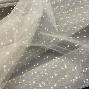 Puede incluir: Tela de tul blanco con pequeños lunares blancos. La tela es transparente y delicada.
