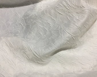 May include: White fabric with a textured, embossed floral pattern. The fabric has a subtle sheen and a soft, drapey feel.