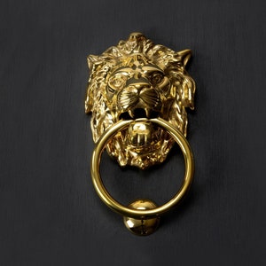 May include: A gold lion's head door knocker with a round ring.