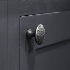 May include: A close-up of a dark grey cabinet door with a hammered metal knob. The knob is round and has a textured surface.