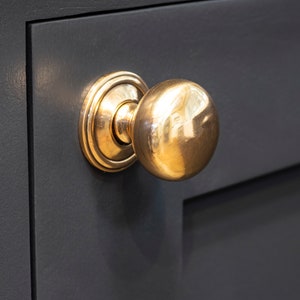 May include: A polished gold door knob with a round, smooth handle and a decorative ring around the base.