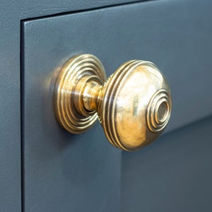 May include: A polished brass door knob with a round, fluted design. The knob is mounted on a dark blue door.