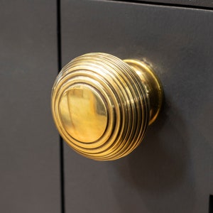 May include: A gold-toned door knob with a round, ribbed design. The knob is mounted on a dark grey door.