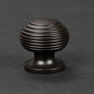 May include: A dark brown, round cabinet knob with a ridged design. The knob has a smooth, rounded base.