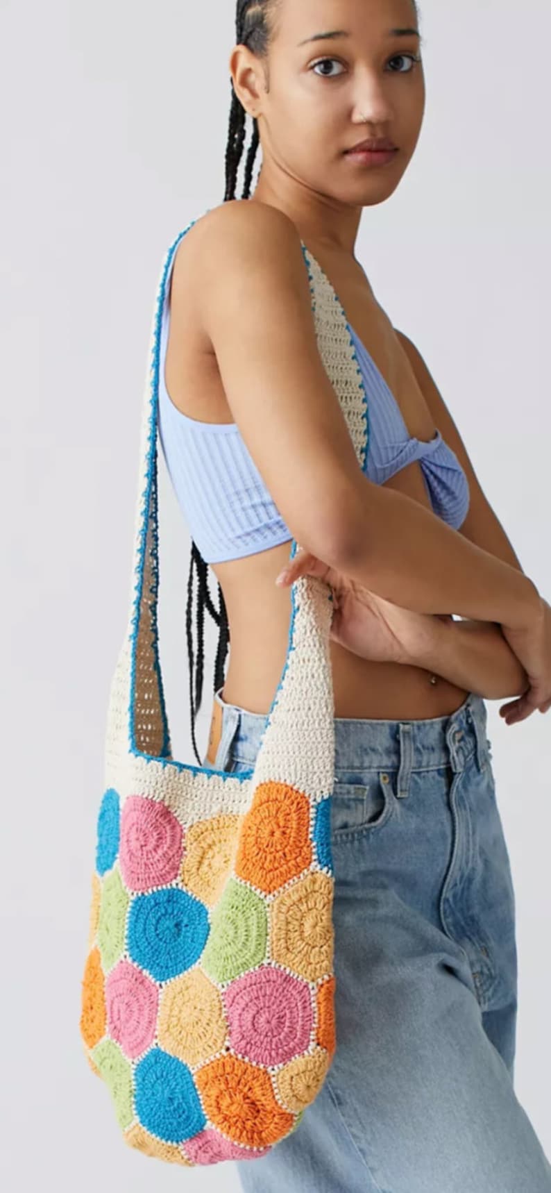 May include: A white crochet tote bag with a colorful geometric pattern. The bag has a long strap and is made of a soft, lightweight material.