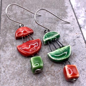 May include: A pair of ceramic earrings with a distinctive design. One earring is red and green, the other green and red. The earrings have a glossy finish and silver-tone ear wires. The earrings are handmade.