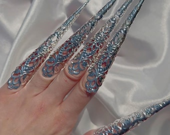 May include: Silver filigree nail rings with pointed tips. The rings are worn on several fingers and are designed to look like long, sharp nails.