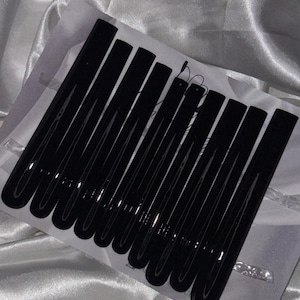Könnte beinhalten: Ein Set mit zehn schwarzen Haarklammern. Die Klammern sind alle gleich groß und haben die gleiche Form und sind in einer Reihe angeordnet. Die Klammern sind aus einem glänzenden, glatten Material.