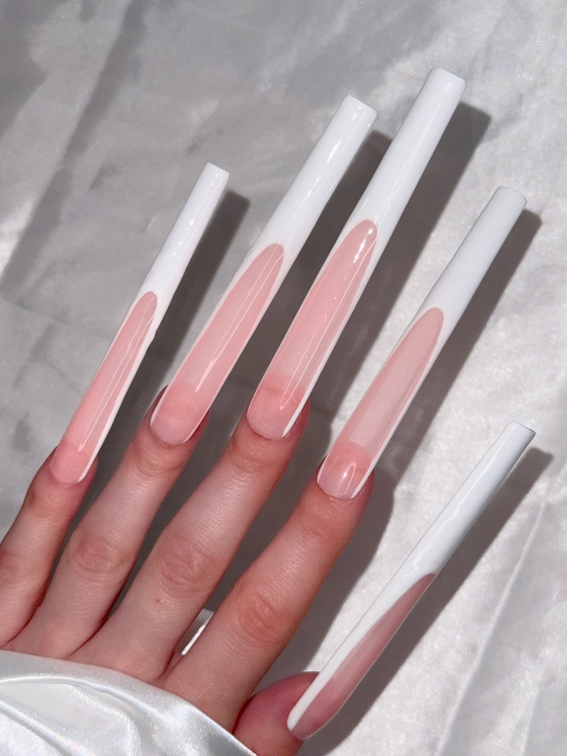 May include: Five long, white, fake nails with a pink base and a white tip. The nails are on a hand.