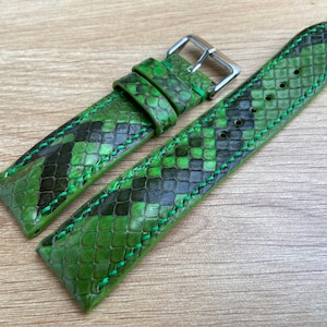 Peut inclure: Un bracelet de montre en peau de serpent vert avec une boucle argentée. Le bracelet est cousu avec du fil vert.