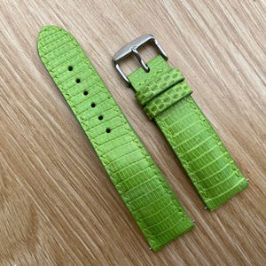 Peut inclure: Bracelets de montre vert vif avec un motif texturé en forme de peau de lézard. L'un des bracelets est doté d'une boucle argentée. Les bracelets sont présentés sur une surface en bois brun clair.