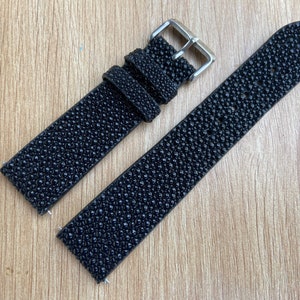 Puede incluir: Correa de reloj negra con una superficie texturizada y punteada. La correa presenta una hebilla plateada y un diseño clásico. La correa del reloj está hecha de un material duradero.