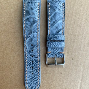 May include: A gray leather watch strap with a light brown stitching and a silver buckle.