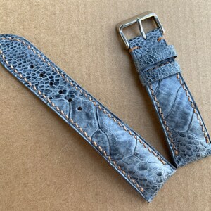 May include: A gray leather watch strap with a light brown stitching detail. The strap is made of a textured material that resembles a reptile skin.