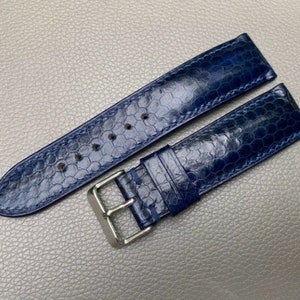 May include: A dark blue leather watch strap with a textured pattern and a silver buckle.