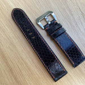 May include: Two black leather watch straps with orange stitching. The straps have a textured, scaly pattern. One strap has a silver buckle.