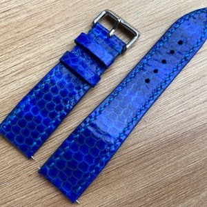 Op de afbeelding: Een blauwe leren horlogeband met een textuurpatroon en witte stiksels. De band is ontworpen voor een horloge met een standaard lugbreedte.