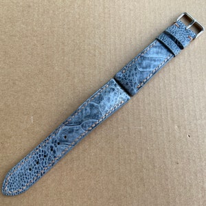 May include: A gray ostrich leather watch strap with orange stitching and silver hardware.