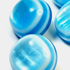 May include: Close-up of several blue and white swirled glass beads. The beads have a rounded, smooth shape and a glossy finish. The color is a mix of light and dark blue with white swirls.