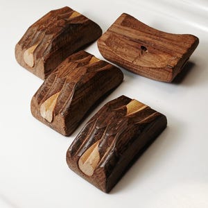 May include: Four handcrafted wooden chopstick rests. Each rest is rectangular with a carved, textured surface in shades of brown and tan. The design features a leaf-like inlay, adding a natural and organic aesthetic. These rests are ideal for Asian-inspired dining.