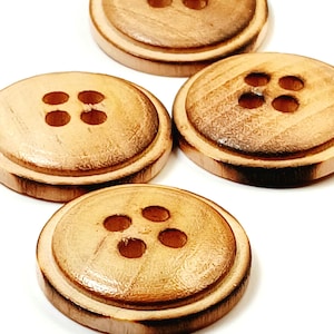 May include: Four round wooden buttons with four holes each. The buttons are light brown with darker brown edges and a natural wood grain pattern. The buttons are arranged on a white background.