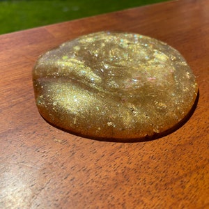 May include: A golden slime with glitter, spread out on a wooden surface.