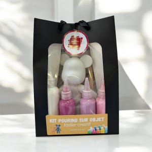 Può includere: Una borsa regalo nera contenente una statuetta di orso bianco, flaconi di vernice rosa e bianca e un pennello. La borsa ha una finestra trasparente e un adesivo rotondo. Il testo sulla borsa recita "KIT POURING SUR OBJET Atelier creatif".