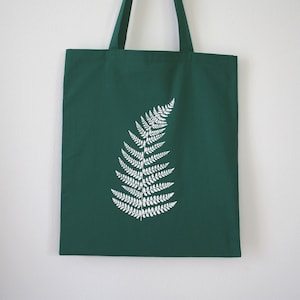Può includere: Una borsa tote verde scuro con un design a felce bianca stampato sul davanti.
