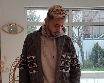 May include: A man wearing a gray knitted cardigan with a white and black geometric pattern, a gray hooded sweatshirt, black pants, and white sneakers.