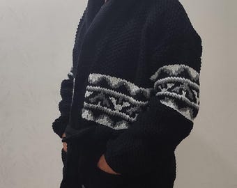May include: A black knitted cardigan with a white and gray geometric pattern on the sleeves and bottom hem. The cardigan has a shawl collar and a tie belt.