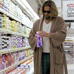 Könnte beinhalten: Eine Person mit Sonnenbrille, weißem Hemd und karierter Hose hält in einem Lebensmittelgeschäft einen Milchkarton. Die Person trägt auch einen braunen Bademantel. Regale mit Lebensmitteln sind im Hintergrund zu sehen.