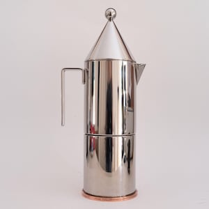 May include: A stainless steel stovetop espresso maker with a conical top and a small handle. The coffee pot has a copper-colored base and a small spout for pouring. The design is sleek and modern.