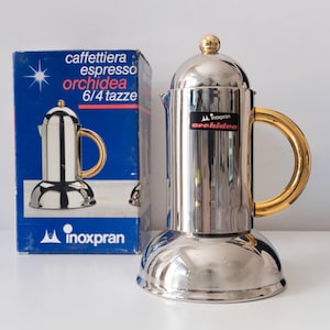 May include: A stainless steel espresso maker with a gold-colored handle and lid knob, next to its blue box. The box reads "caffettiera espresso orchidea 6/4 tazze" and features a starburst graphic. The brand name "inoxpran" is also visible.