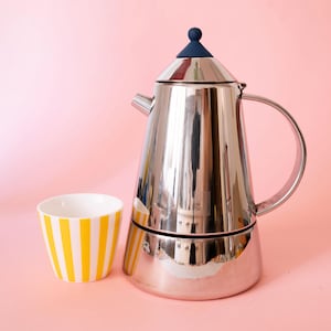 以下が含まれることがあります： 円錐形の本体、湾曲したハンドル、蓋に小さなダークブルーのつまみが付いたステンレス製の光沢のあるエスプレッソメーカーと、外側に縦の黄色いストライプが入った白いセラミック製のカップが並んでいます。