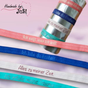 Könnte beinhalten: Eine Auswahl an elastischen Haarbandern in verschiedenen Farben, jeweils mit einem deutschen Spruch versehen. Die Haarbänder sind in Rosa, Blau, Weiß und Türkis gehalten. Sätze wie "Ich weiß, was ich will" und "Ich liebe die Freiheit."