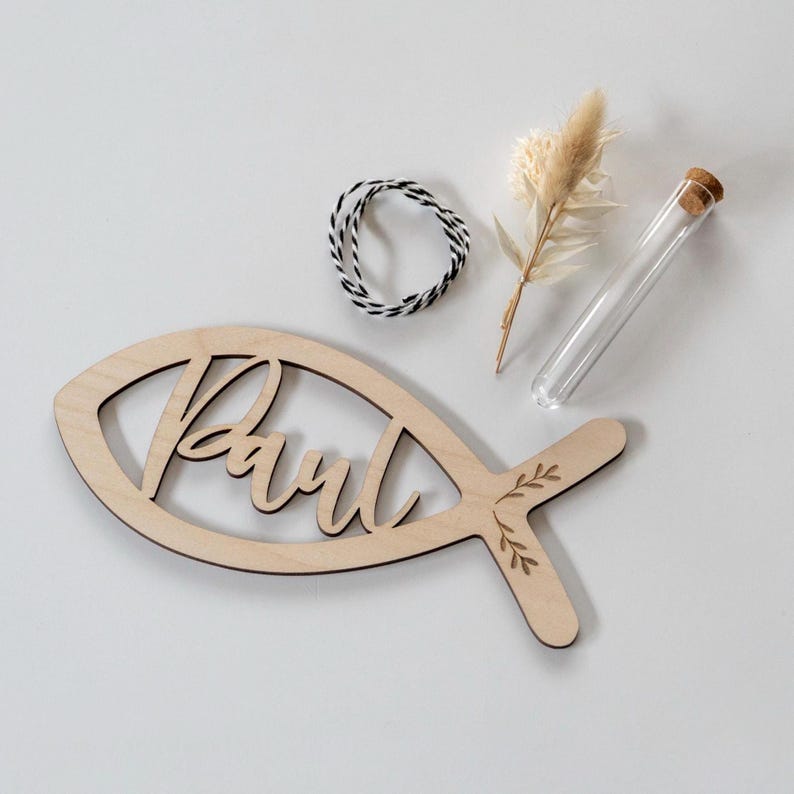 K&ouml;nnte beinhalten: Holzdekor in Fischform mit dem Namen "Paul" in Schreibschrift ausgeschnitten. Der Fisch hat ein Blattmuster auf dem Schwanz. Enth&auml;lt auch ein Glasr&ouml;hrchen mit Korken, Trockenblumen und schwarz-wei&szlig;em Bindfaden.