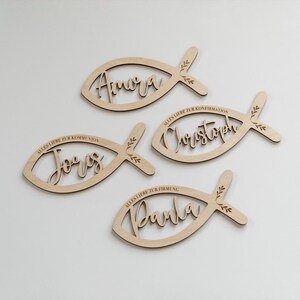 K&ouml;nnte beinhalten: Vier Holzdekorationen in Fischform mit Namen und S&auml;tzen auf Deutsch. Jeder Fisch hat einen Namen in Schreibschrift: Amora, J&ouml;rg, Christoph und Darla. Die S&auml;tze beinhalten "Alles Liebe zur Konfirmation" und "Alles Liebe zur Kommunion".